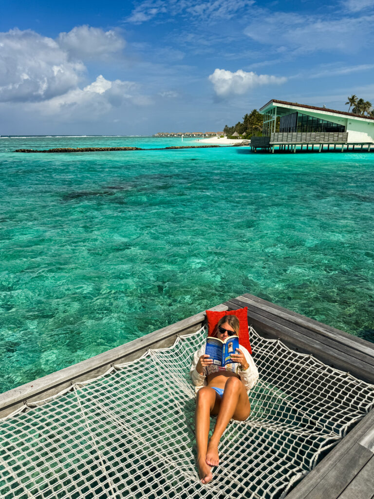 Guest reading in a hammock over a clear lagoon